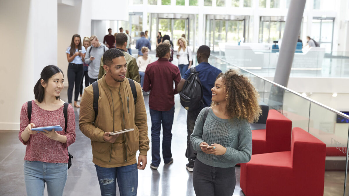 Students holding tablets and phone talk in university lobby