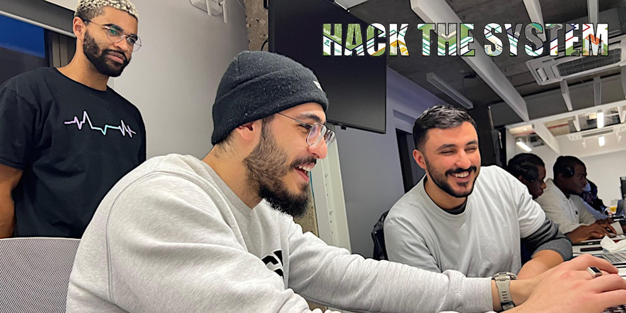 Three men looking at a laptop smiling in a meeting room for the Hack the System event