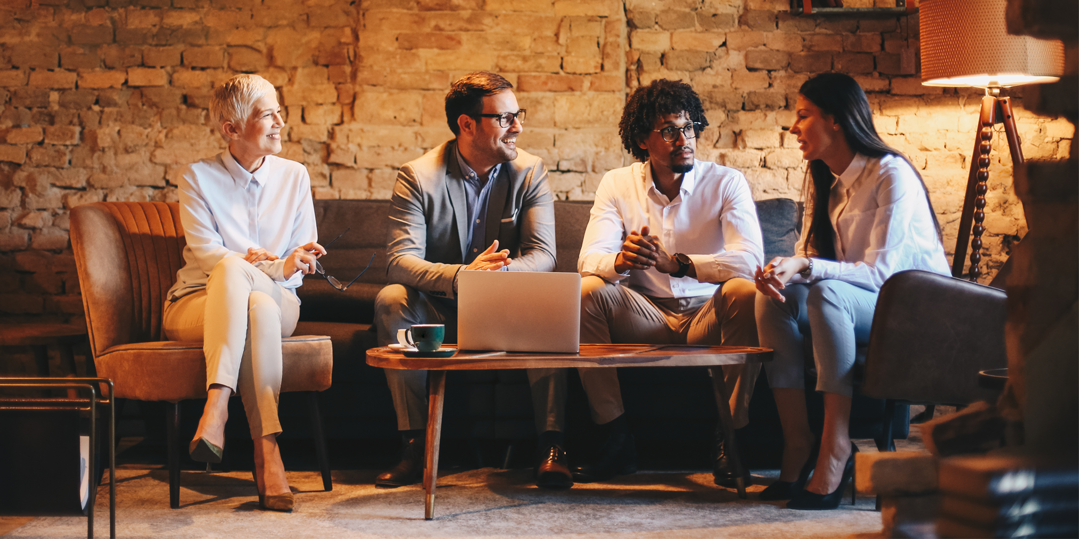 Group of business professionals smiling and talking over a laptop in a cafe